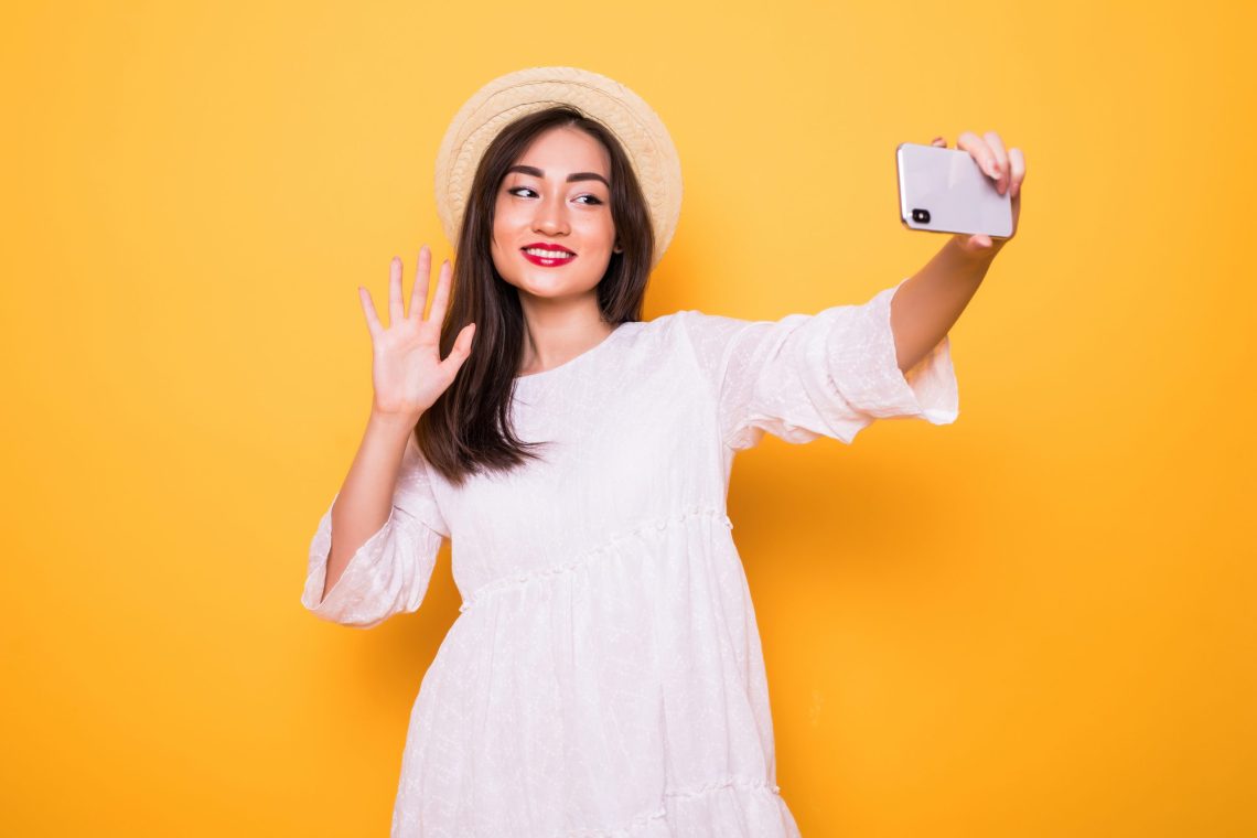 Young Asian woman selfie with mobile phone on yellow background